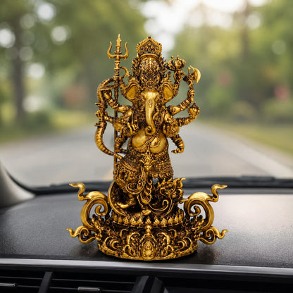 An ornate gold-toned Ganesha figurine displayed on a car dashboard with a blurred road and trees in the background.